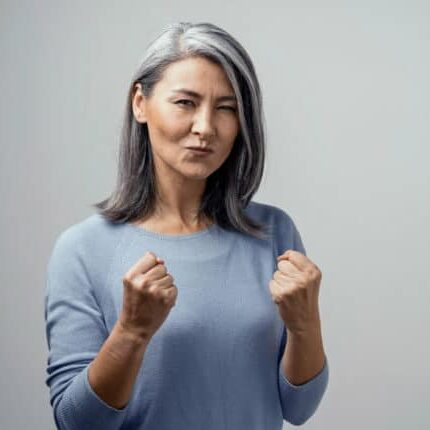 Happy Mature Asian Female Model Smiles Happily. She Celebrates Victory and Holds Fists in Satisfaction. Hand Photo in Studio on White Background